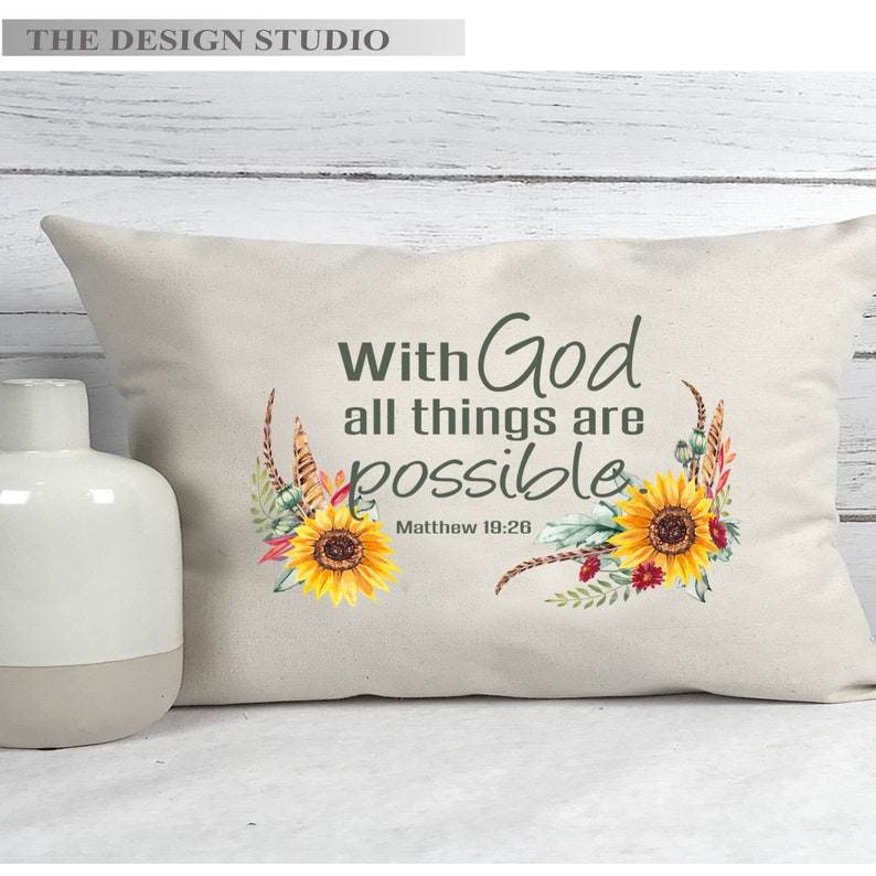 Pu&ograve; includere: Un cuscino bianco con il testo "With God all things are possible" e il riferimento biblico "Matthew 19:26". Il cuscino &egrave; decorato con un motivo floreale con girasoli e fiori rossi.