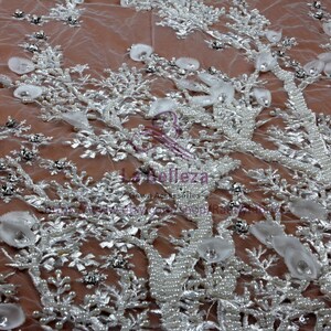 May include: White beaded lace fabric with a floral design. The fabric is embellished with pearls, sequins, and small white flowers. The fabric is sheer and delicate.