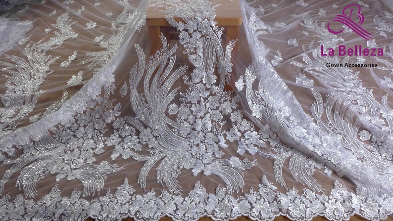 May include: White tulle fabric with silver glitter and floral embroidery. The fabric has a delicate, feminine look and would be perfect for a wedding dress or other special occasion garment.