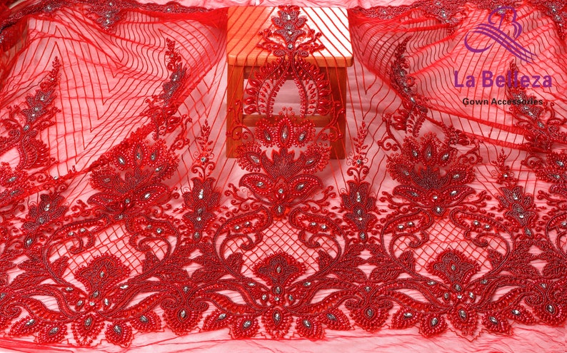 May include: Red beaded lace fabric with a floral design. The fabric is sheer and has a delicate texture. The beads are small and evenly spaced. The fabric is perfect for making dresses, skirts, and other garments.
