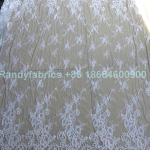 May include: White lace fabric with a delicate floral pattern. The lace is sheer and has a soft, flowing texture.