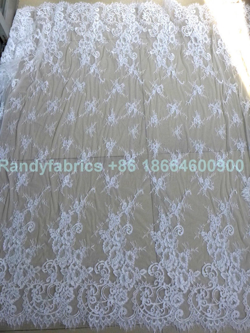 May include: White lace fabric with a delicate floral pattern. The lace is sheer and has a soft, flowing texture.