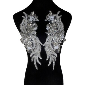 May include: Two silver beaded and sequined appliques with a symmetrical design. The appliques feature clear and silver beads, sequins, and small white floral accents. They are displayed on a black mannequin.