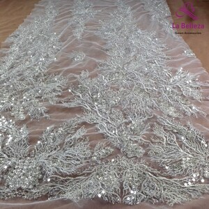 May include: White tulle fabric with silver sequins and beads in a floral pattern. The fabric is sheer and delicate, with a soft, flowing texture. La Belleza Gown Accessories is printed in the top right corner.