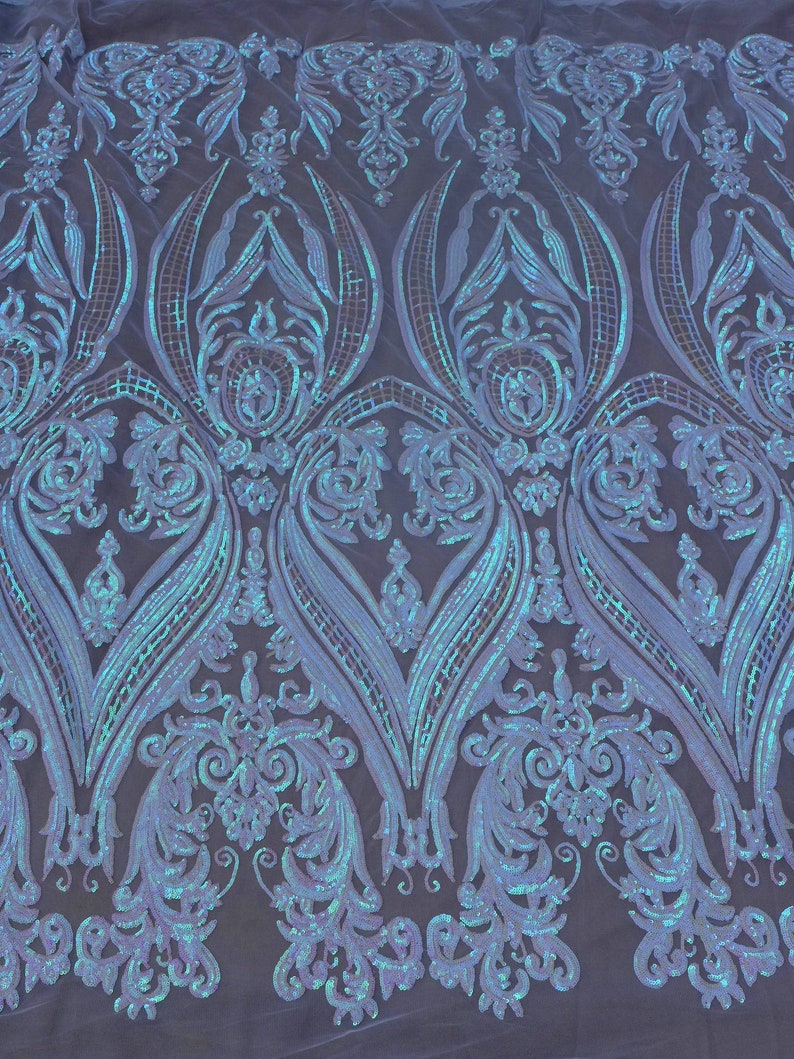 May include: A close-up of iridescent blue and white sequined fabric with a damask pattern. The fabric is sheer and has a delicate, feminine feel.