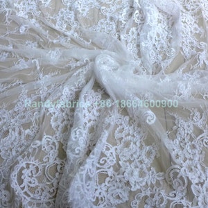 May include: White lace fabric with a delicate floral pattern. The lace is soft and sheer, and it would be perfect for a variety of projects, such as wedding dresses, tablecloths, and curtains.