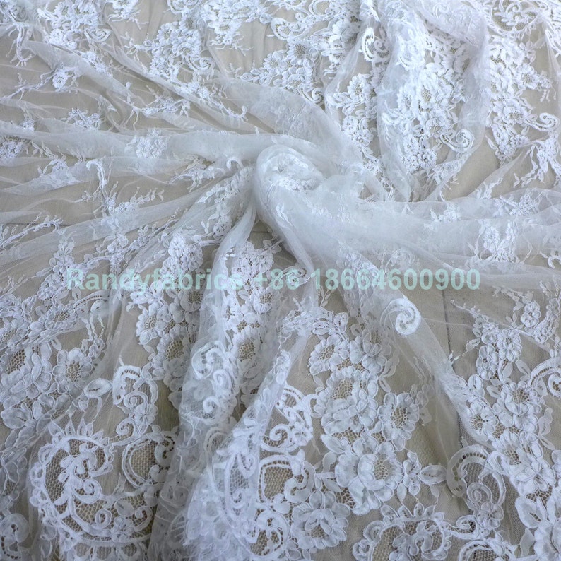 May include: White lace fabric with a delicate floral pattern. The lace is soft and sheer, and it would be perfect for a variety of projects, such as wedding dresses, tablecloths, and curtains.