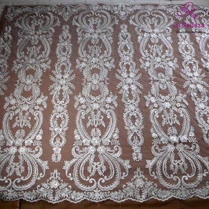 K&ouml;nnte beinhalten: Wei&szlig;er, gestickter Spitzenstoff mit einem Blumenmuster. Der Stoff hat ein zartes, filigranes Design mit kleinen Blumen und Bl&auml;ttern.