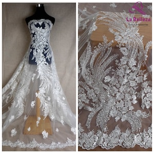 May include: White tulle fabric with silver sequins and floral embroidery. The fabric is shown draped over a dress form and laid flat.
