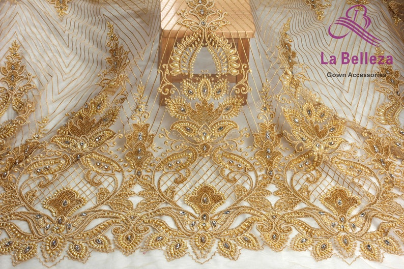 May include: Gold beaded lace fabric with a delicate floral pattern. The fabric is sheer and has a subtle shimmer. It is perfect for adding a touch of elegance to any project.