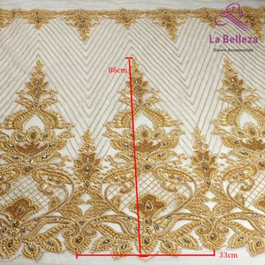 May include: Gold beaded lace fabric with a geometric pattern. The fabric is 86 inches long and 33 inches wide.