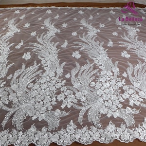 May include: White beaded lace fabric with a floral design. The fabric has a delicate, sheer texture and is perfect for adding a touch of elegance to any project.