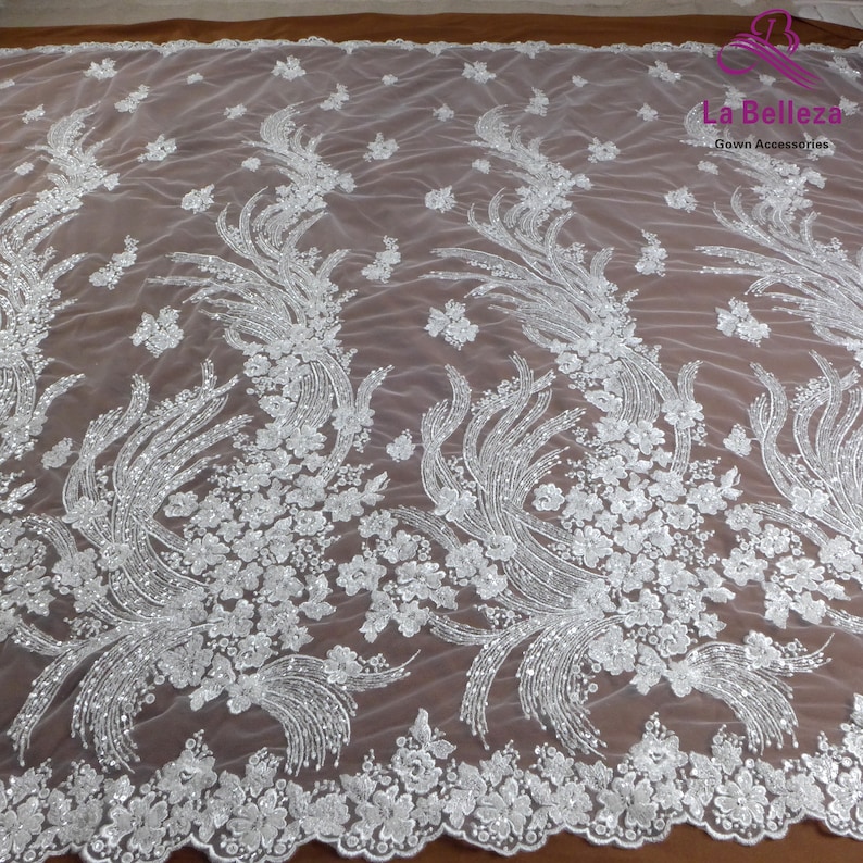 May include: White beaded lace fabric with a floral design. The fabric has a delicate, sheer texture and is perfect for adding a touch of elegance to any project.