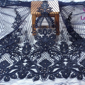 May include: Navy blue beaded lace fabric with a floral design. The fabric is sheer and has a delicate texture. The beads are small and evenly spaced.