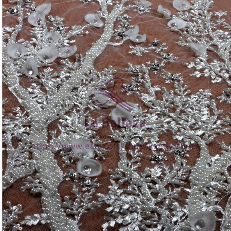 May include: White beaded lace fabric with a floral design. The fabric is sheer and has a delicate, feminine look.
