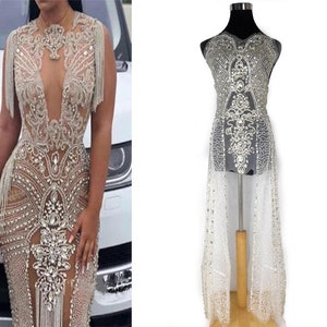 Può includere: Un tessuto trasparente, perlato e paillettes con scollo a V profondo e dettagli di frange. Il tessuto è progettato per essere utilizzato come abito o top.