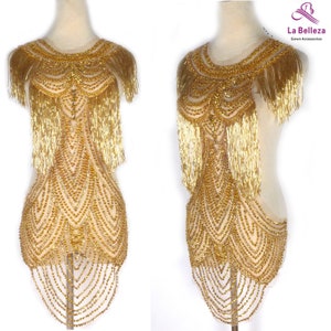 Könnte beinhalten: Goldene Perlen- und Fransenverzierung für ein Kleid oder ein Kleidungsstück. Die Verzierung hat ein zartes, filigranes Design mit kaskadierenden Fransen.