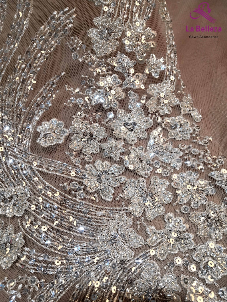 May include: Close-up of a silver sequined fabric with a floral design. The fabric is sheer and has a delicate, feminine look.