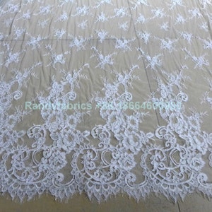 May include: White floral lace fabric with a delicate pattern. The lace has a scalloped edge and is perfect for crafting, sewing, or decorating.