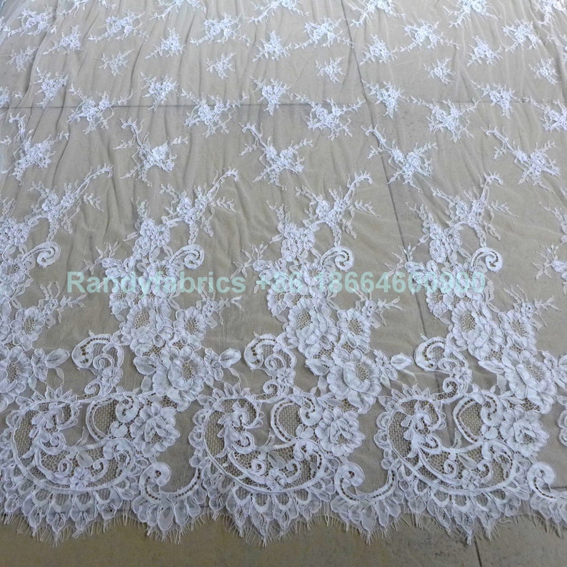May include: White floral lace fabric with a delicate pattern. The lace has a scalloped edge and is perfect for crafting, sewing, or decorating.