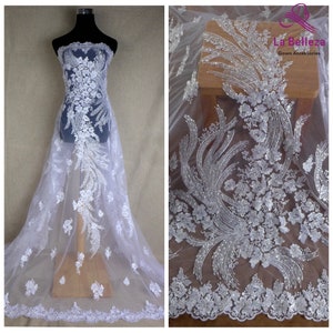 May include: White beaded lace fabric with a floral design. The fabric is sheer and has a delicate, feminine look. It is perfect for adding a touch of elegance to any project.