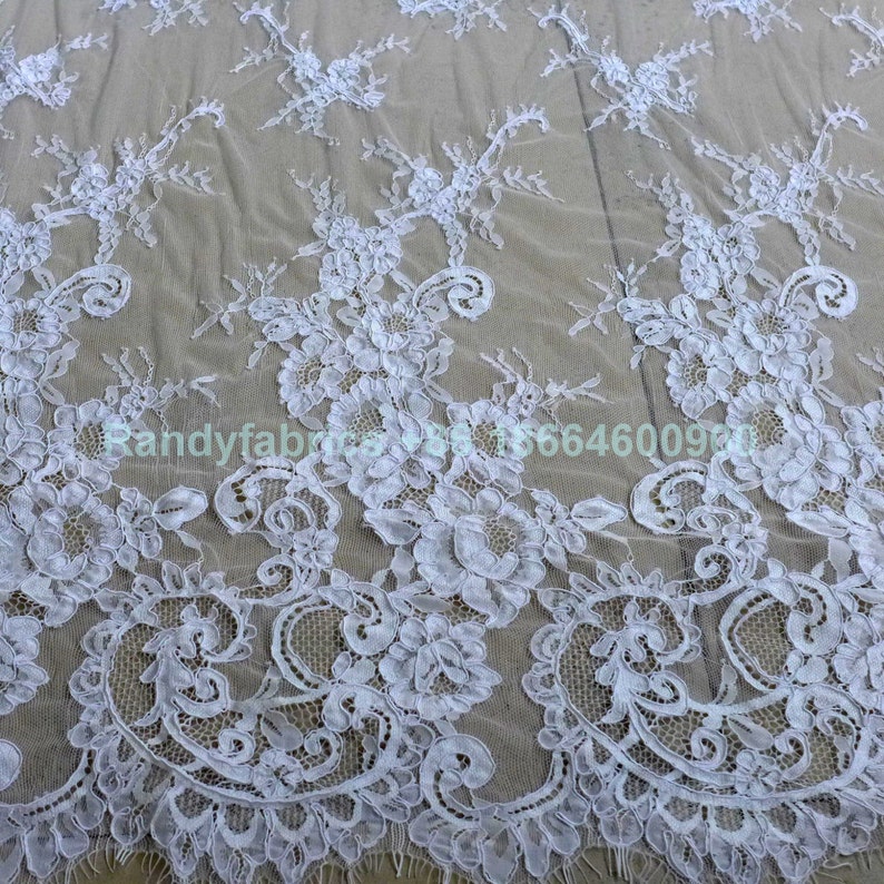 May include: White lace fabric with a delicate floral pattern. The lace is sheer and has a soft, flowing texture.