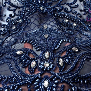 May include: Navy blue beaded lace fabric with a floral design and clear rhinestones. The fabric is sheer and has a delicate texture.