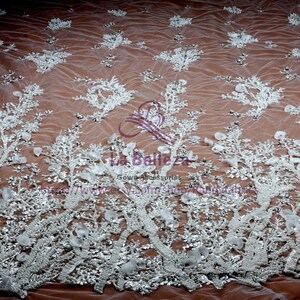 May include: White beaded lace fabric with a floral design. The fabric is sheer and has a delicate, feminine look. It is perfect for wedding dresses, evening gowns, and other special occasion garments.