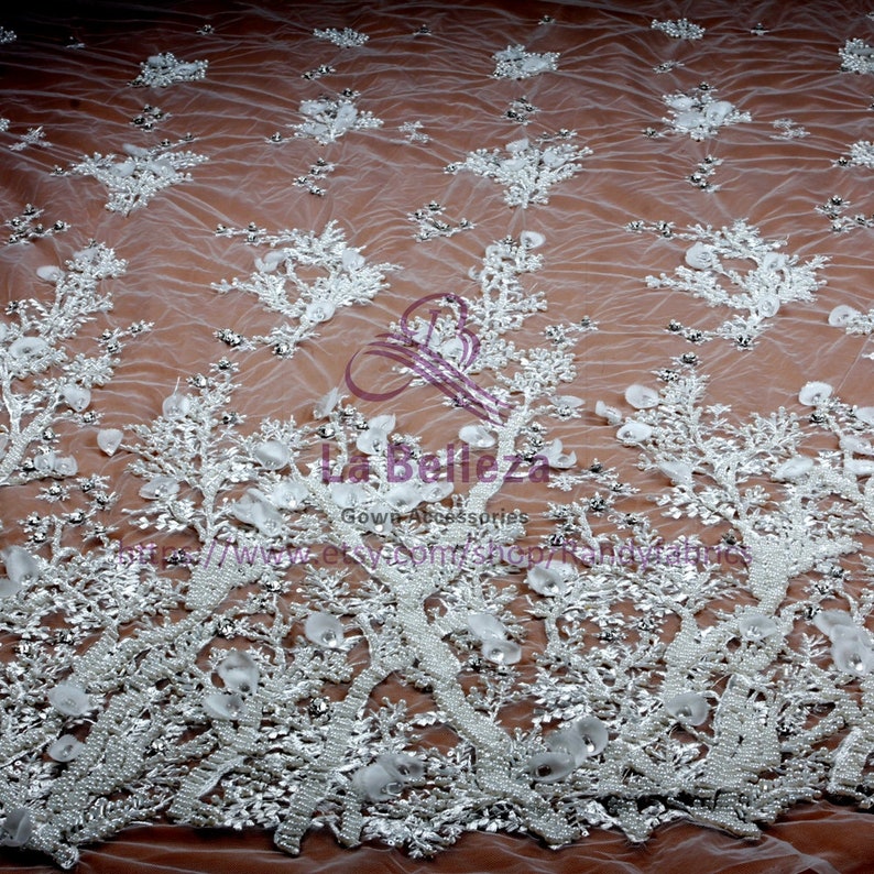 May include: White beaded lace fabric with a floral design. The fabric is sheer and has a delicate, feminine look. It is perfect for wedding dresses, evening gowns, and other special occasion garments.