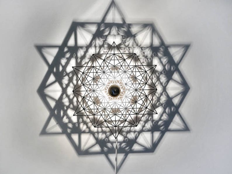 May include: A black metal geometric light fixture casts a shadow of a starburst pattern on a white ceiling.