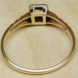 May include: A gold ring with a square-shaped gemstone set in a bezel setting. The ring has a simple band with a delicate design.