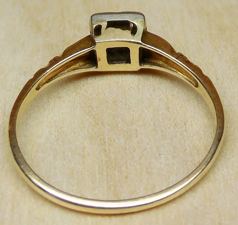 May include: A gold ring with a square-shaped gemstone set in a bezel setting. The ring has a simple band with a delicate design.