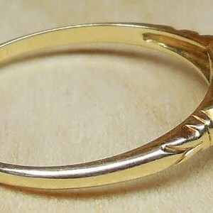 May include: A gold ring with a single diamond set in a square bezel. The ring has a delicate band with a decorative design.