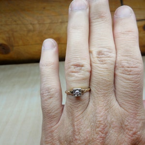May include: A gold ring with a single, clear diamond set in a square shape.