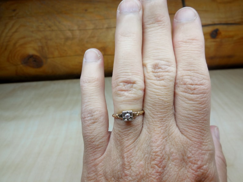 May include: A gold ring with a single, clear diamond set in a square shape.