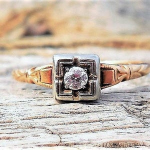 May include: A vintage engagement ring with a single round diamond set in a square platinum setting. The band is yellow gold and has a delicate, ornate design.