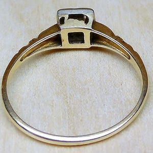 May include: A gold ring with a square-shaped stone set in the center. The ring is simple and elegant.