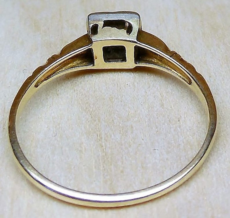 May include: A gold ring with a square-shaped stone set in the center. The ring is simple and elegant.