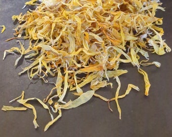 May include: A pile of dried yellow flower petals, likely calendula, on a dark gray surface.