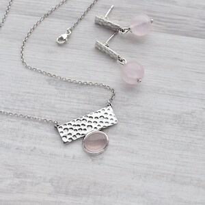 May include: A silver necklace with a hammered rectangular pendant and a pink rose quartz stone. Matching earrings with hammered silver posts and pink rose quartz stones.