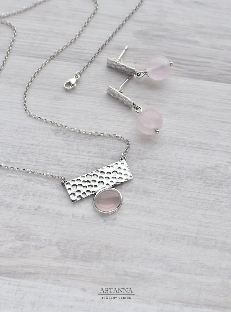May include: A silver necklace with a hammered rectangular pendant and a pink rose quartz stone. Matching earrings with hammered silver posts and pink rose quartz stones.