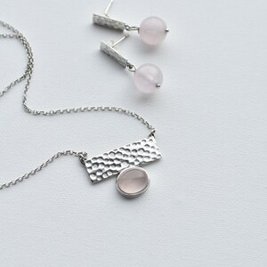 May include: A silver necklace with a hammered rectangular pendant and a pink rose quartz stone. Matching earrings with hammered silver posts and pink rose quartz stones.