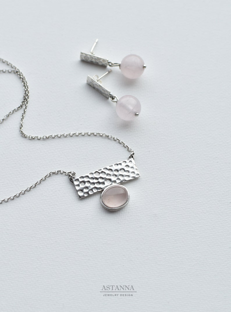 May include: A silver necklace with a hammered rectangular pendant and a pink rose quartz stone. Matching earrings with hammered silver posts and pink rose quartz stones.