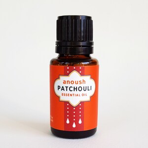 May include: A small amber glass bottle with a black cap and a red label. The label says "anoush PATCHOULI ESSENTIAL OIL" and has a white border with a dotted pattern. There are three white raindrops on the label.