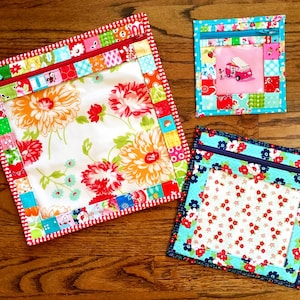 May include: Three zippered pouches with colorful patchwork fabric and a clear vinyl window. The pouches are lined with a white floral fabric and have a zipper closure.
