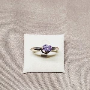 Könnte beinhalten: Ein silberner Ring mit einem violetten Edelstein, der in einem dekorativen Design gefasst ist.