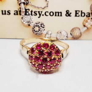 May include: A gold ring with a cluster of small, deep red ruby stones set in a circular pattern.