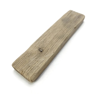 May include: A rectangular piece of weathered driftwood with a light gray, textured surface and a visible knot in the center. The wood grain is prominent, showing natural lines and grooves across the entire length of the flat, elongated object.
