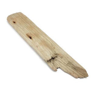 May include: A piece of driftwood, light brown in color, with a natural, weathered appearance. The wood has visible grain and two small holes. The end of the wood is jagged, and the overall shape is long and narrow.