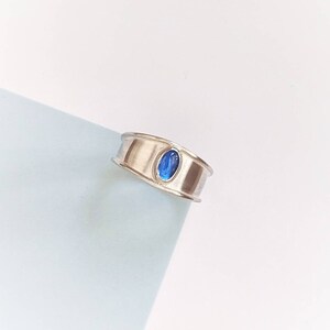 May include: A silver ring with a blue oval-shaped gemstone set in the centre.